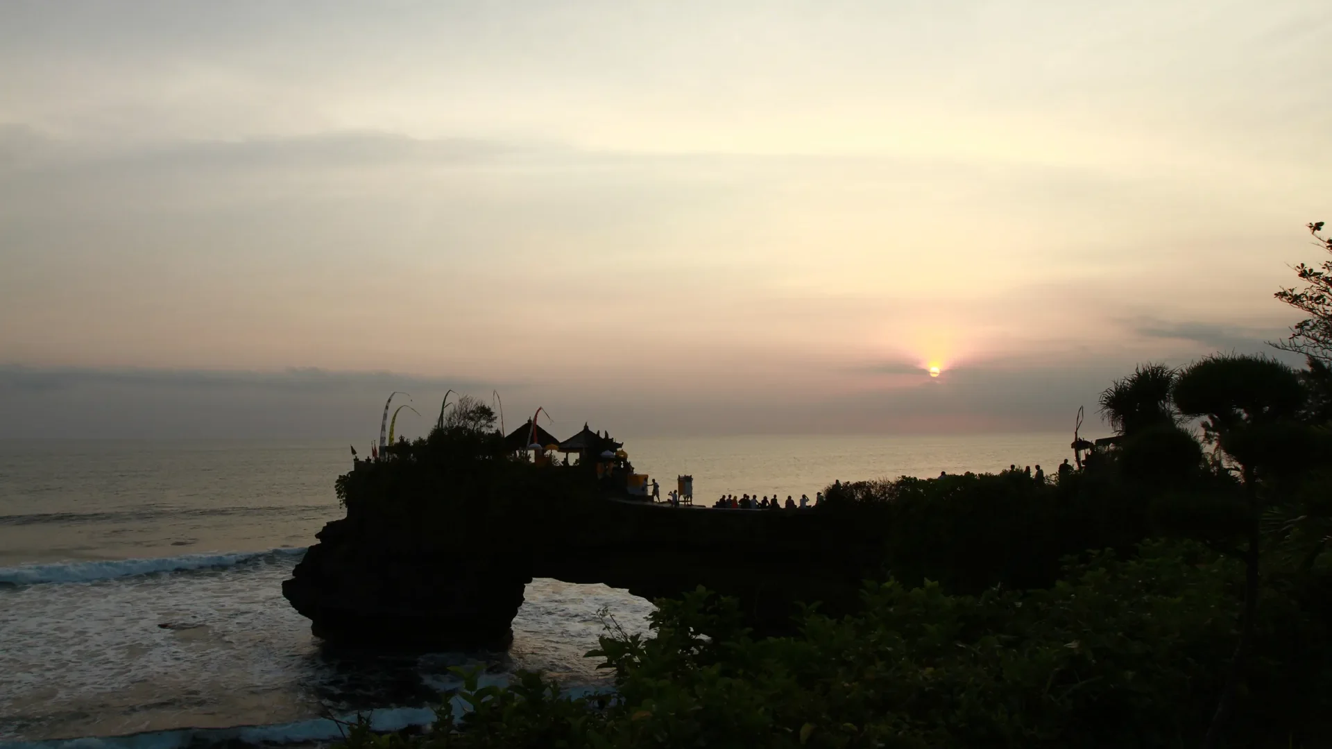 Siluet Pura Tanah Lot di tepi laut Bali saat matahari terbenam