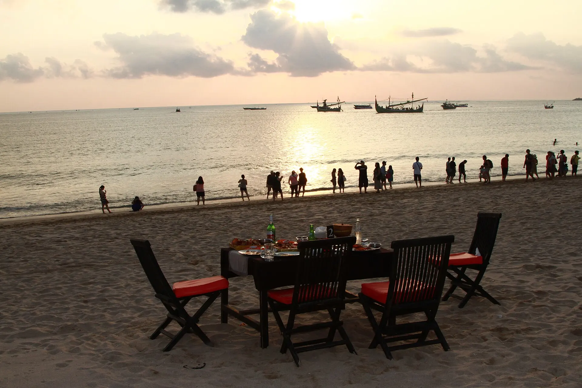 Meja makan berjajar di tepi Pantai Jimbaran menjelang matahari terbenam